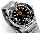 Wristwatch close-up with black dial, orange hands, and stainless mesh bracelet