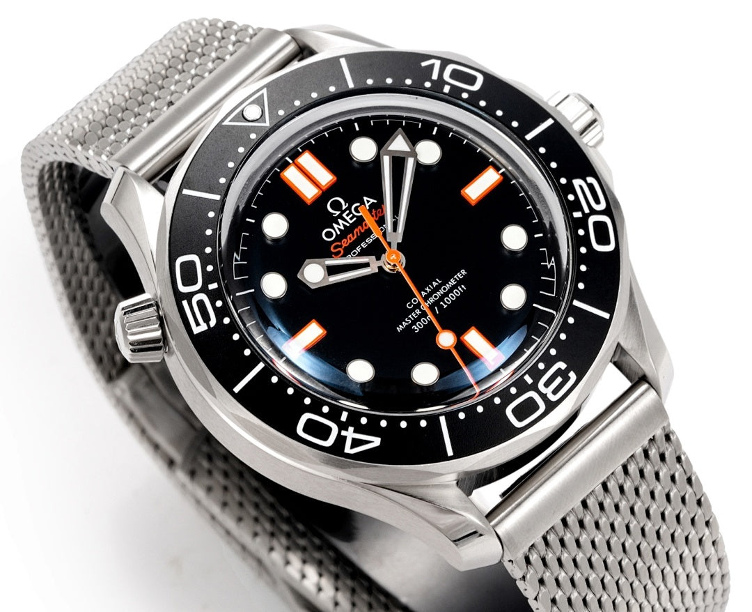 Wristwatch close-up with black dial, orange hands, and stainless mesh bracelet