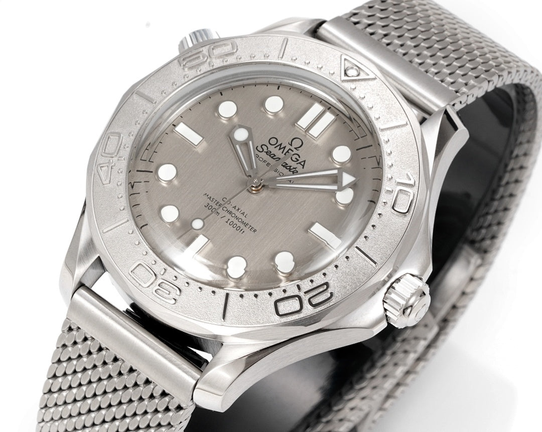 Stainless steel diver watch dial with crown and gray mesh bracelet, angled front view.