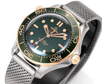 Omega watch close-up with green dial, gold bezel numerals, metal mesh bracelet
