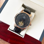 Omega De Ville wristwatch in box with dark dial, rose-gold case, black leather strap.