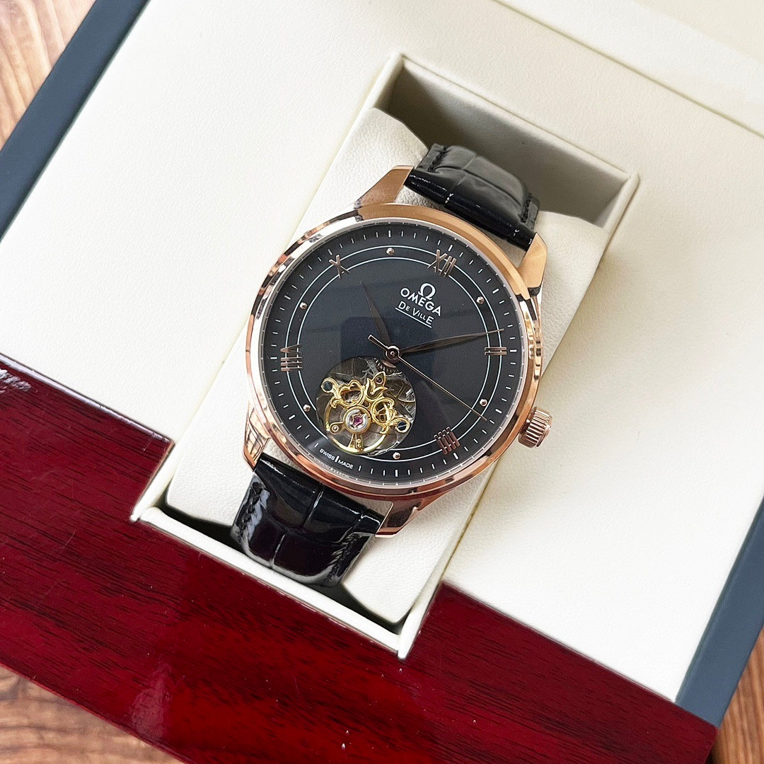 Omega De Ville wristwatch in box with dark dial, rose-gold case, black leather strap.