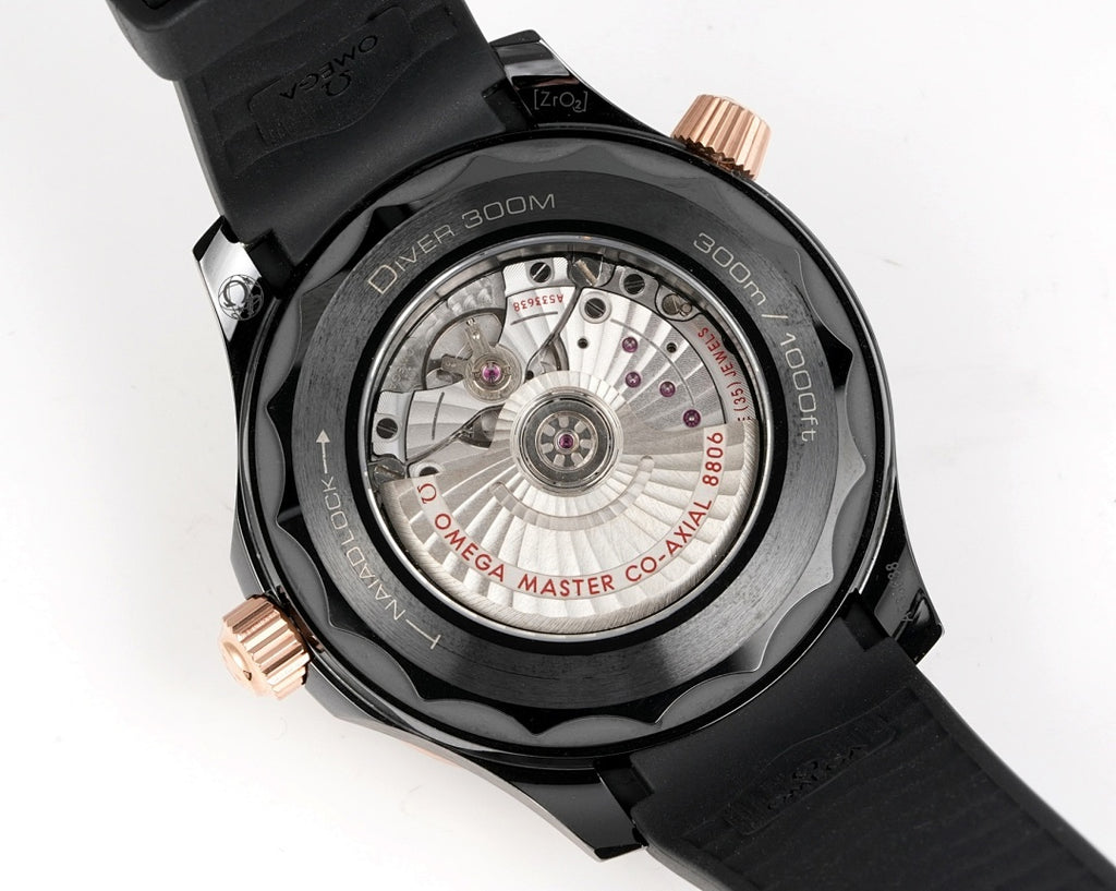 Black diver watch caseback with visible mechanical movement and rose-gold crown accents.