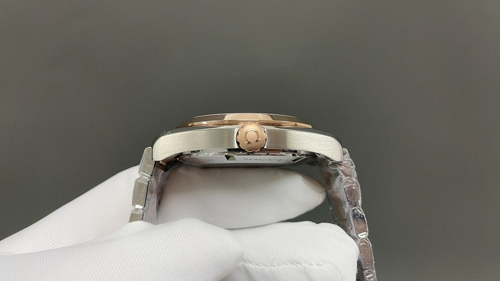 Steel wristwatch caseback detail with gold-toned crown, held by white glove