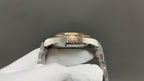 Steel wristwatch caseback detail with gold-toned crown, held by white glove