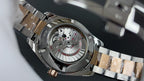 Steel wristwatch with open caseback showing mechanical movement and bracelet