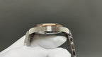Steel wristwatch caseback with gold-toned bezel ring, held by white glove