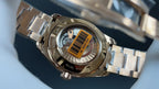 Gold wristwatch with steel bracelet, see-through caseback with barcode sticker visible