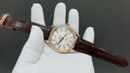 Analog wristwatch with white dial and brown leather strap, angled on display