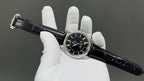 Omega watch with dark dial and black leather strap, crown visible