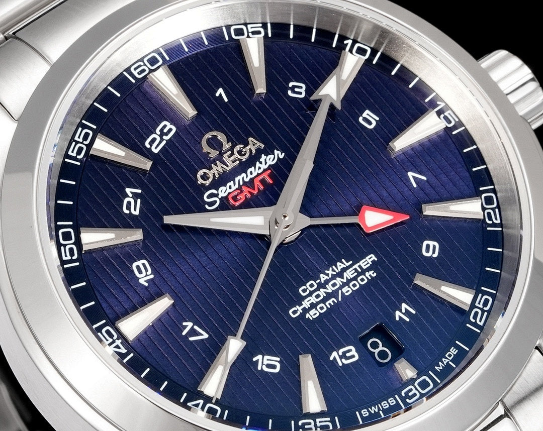 Close-up of blue watch dial with silver hands, logos, and minute markers on a sunray texture.