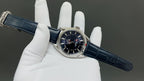 Wristwatch on blue leather strap held in gloves, silver case and dark dial