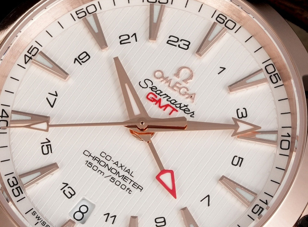 Omega wristwatch dial close-up with white face, hour markers, and red GMT hand.