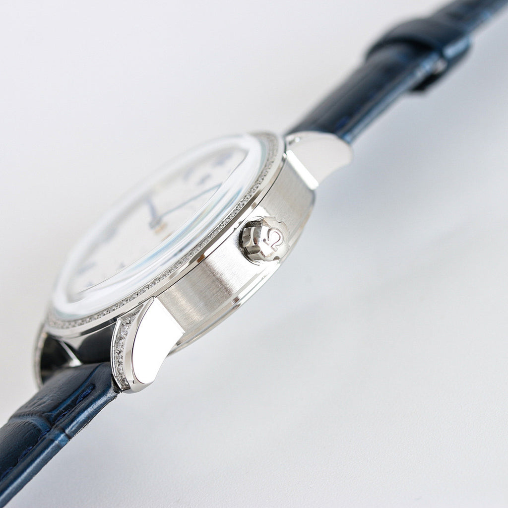 Silver watch case detail with blue leather strap; polished metal with crown and bezel stones.