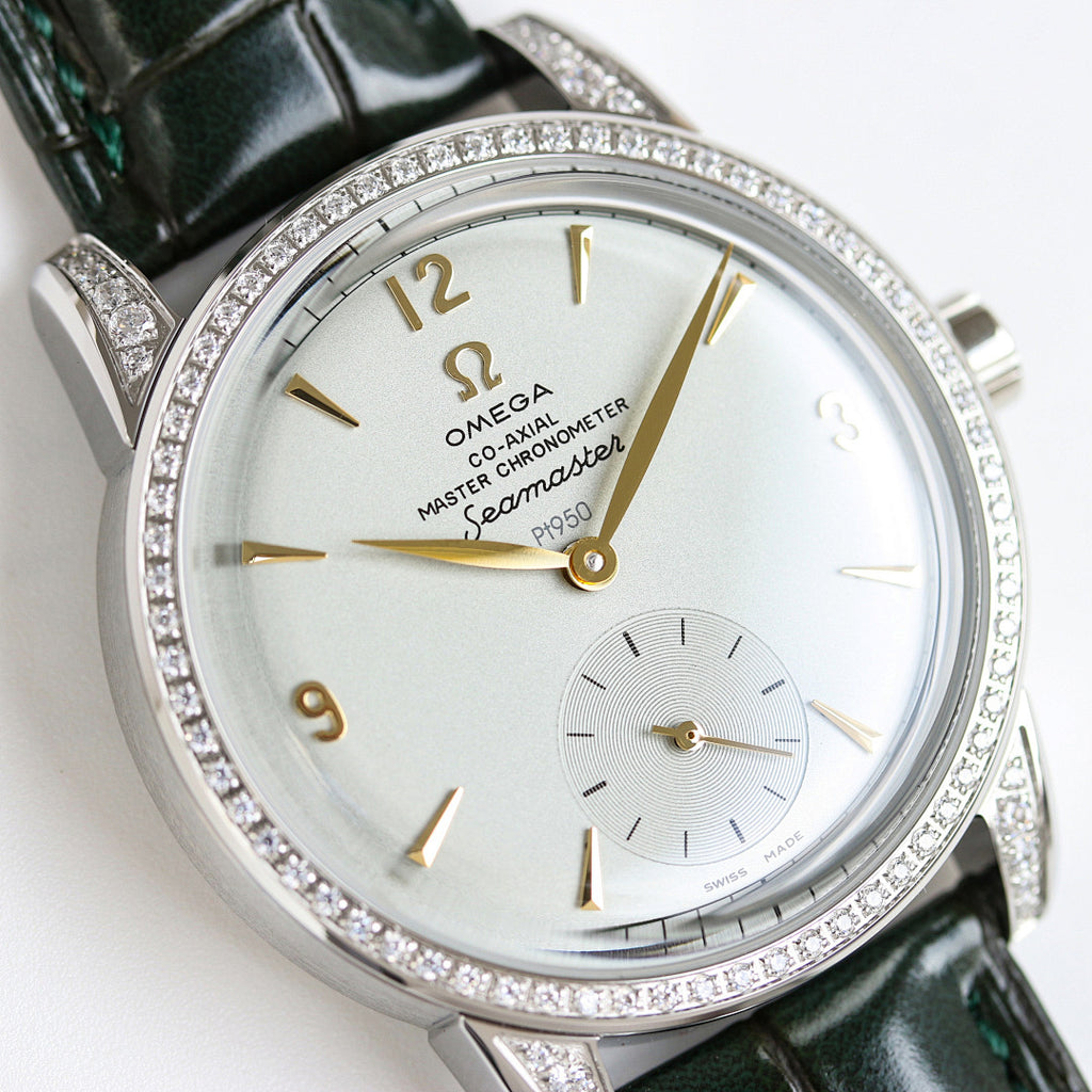 Silver watch close-up with green leather strap, diamond bezel, gold details on white dial.