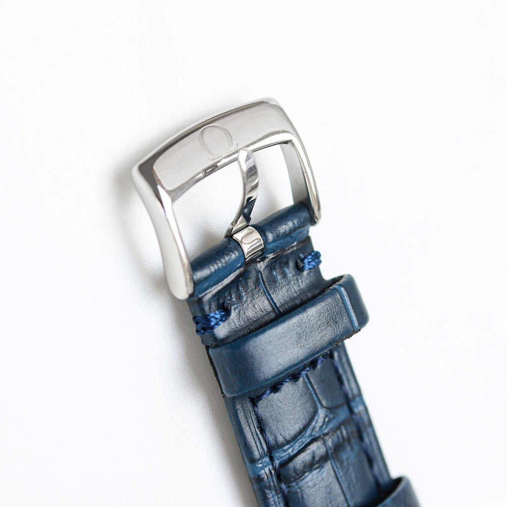 Silver watch case with blue leather strap, side view.