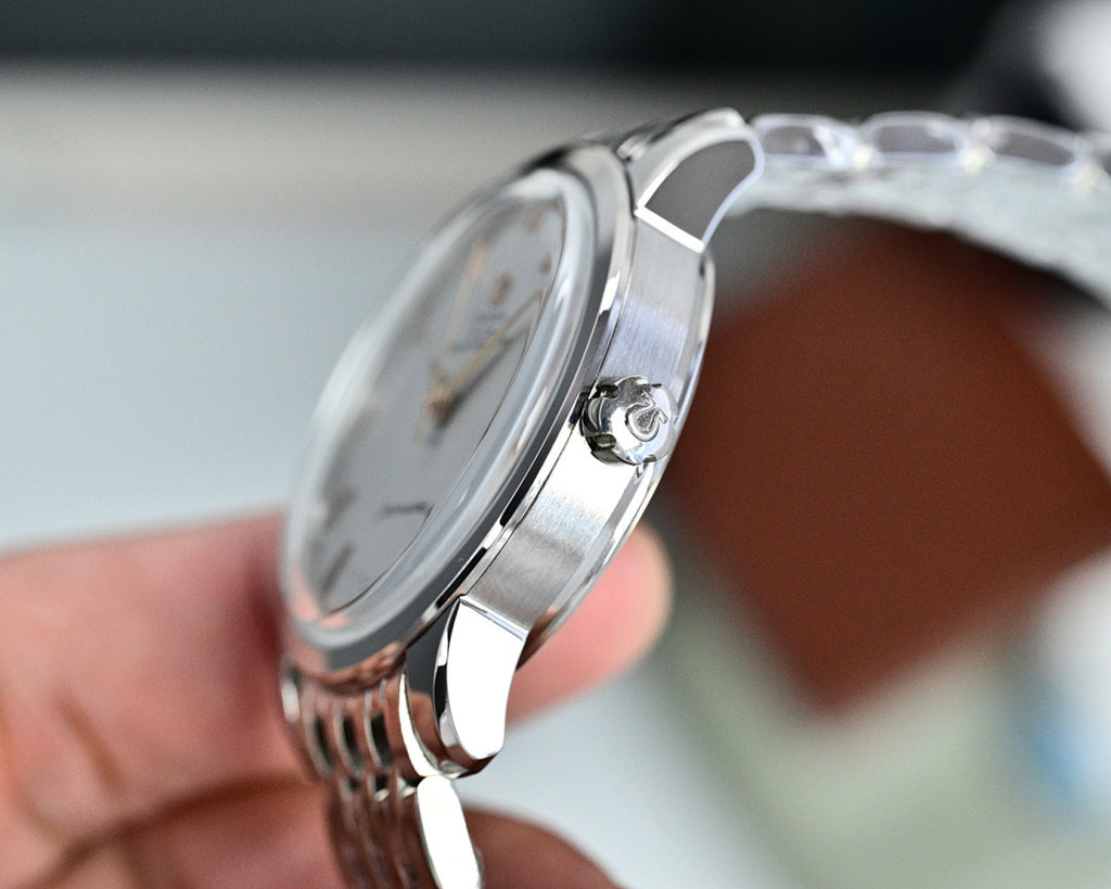 Silver wristwatch side view with crown and metal bracelet, held in a hand