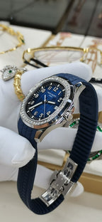 Patek Philippe watch on blue strap with blue dial and jeweled bezel, clasp visible.