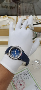 Patek Philippe watch on hand with blue dial and blue rubber strap, on display stand.
