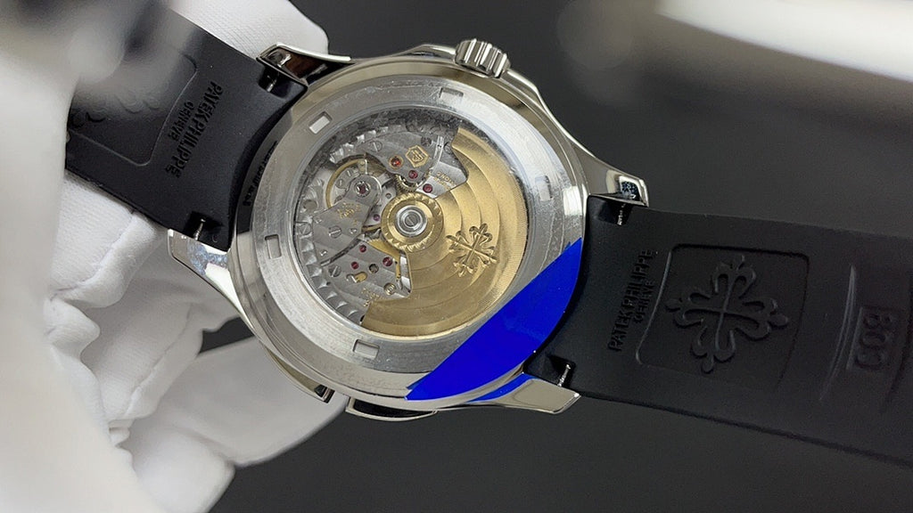 Patek Philippe watch open caseback on black rubber strap, gold-toned movement visible