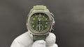 Round wristwatch with green dial, silver-tone case, and green rubber strap on white gloves