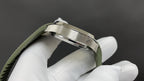 Wristwatch side profile with silver-tone case and green rubber strap held by white gloves
