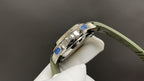 Wristwatch side view with blue accents on bezel, green rubber strap, silver-tone case