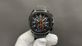 Patek Philippe wristwatch with black dial, orange hands, and black steel bracelet