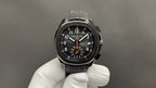 Patek Philippe wristwatch on gloved hand with black dial, orange hands, and black bracelet