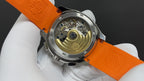 Patek Philippe wristwatch open case on orange strap, showing mechanical movement.