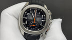 Patek Philippe watch with black dial, orange chronograph hands, black strap, steel case