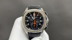 Patek Philippe watch front view with black dial, orange hands, steel bezel, black strap