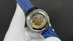 Patek Philippe wristwatch case with visible mechanical movement, blue leather strap.