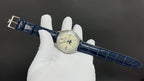 Patek Philippe wristwatch on glove, blue leather strap with buckle, cream dial.