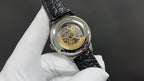 Wristwatch with black crocodile-texture leather strap and see-through caseback showing gears