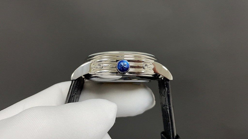 Wristwatch crown and blue gemstone detail on polished stainless steel case with black leather strap