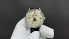 Stainless steel wristwatch with cream dial, Roman numerals, black leather strap in gloved hand