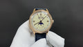 Patek Philippe watch with blue leather strap and gold-tone case, cream dial and roman numerals.
