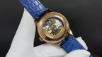 Patek Philippe watch with blue leather strap and gold-tone case, open view of movement.