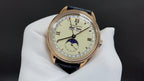 Patek Philippe watch with blue leather strap and gold-tone case, cream dial with roman numerals.