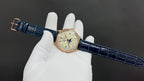 Patek Philippe watch with blue leather strap and gold-tone case held on white gloves.