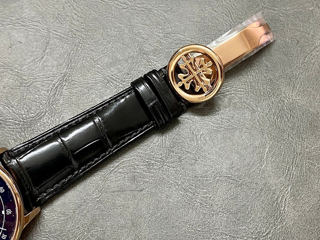 Patek Philippe wristwatch crown with gold emblem, black leather strap