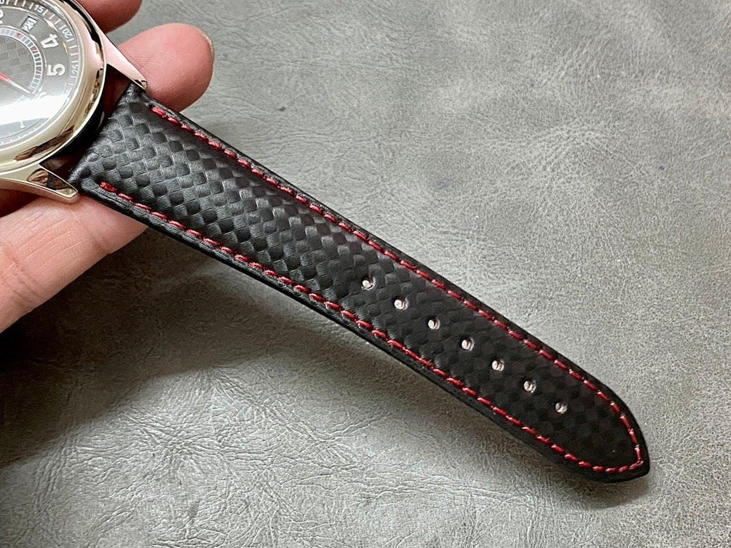 Black carbon-textured leather watch strap with red stitching and black underside