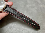 Black carbon-textured leather watch strap with red stitching and black underside