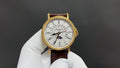 Patek Philippe watch with white dial, gold-tone case, brown leather strap.