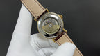 Patek Philippe watch with open back, gold-tone case, brown leather strap.