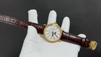 Patek Philippe watch on brown leather strap with gold-tone bezel, white dial.