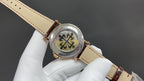 Patek Philippe watch angled view; gold crown, brown leather strap with buckle, on glove.