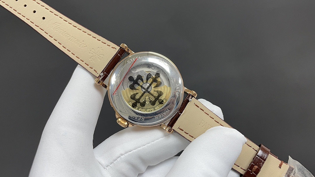 Patek Philippe watch angled view; gold crown, brown leather strap with buckle, on glove.