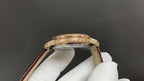 Patek Philippe watch case close-up with gold bezel and crown, brown leather strap.